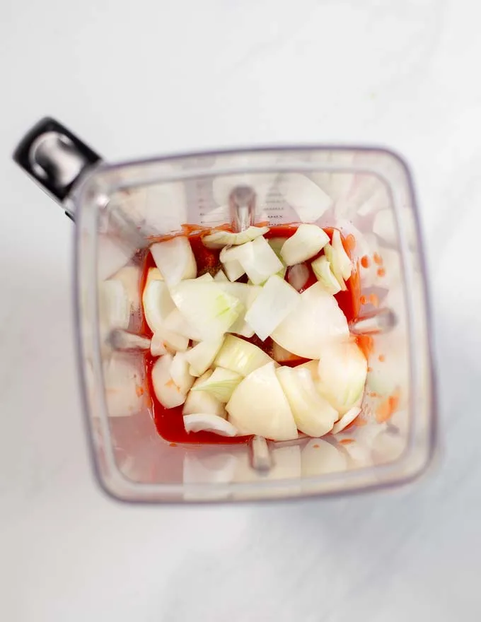 Top view into a bowl of a blender, showing the ingredients for the tomato broth.