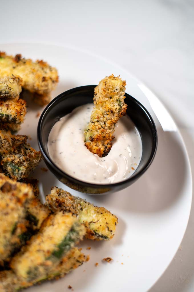 A single Zucchini Fry is dipped into sauce.