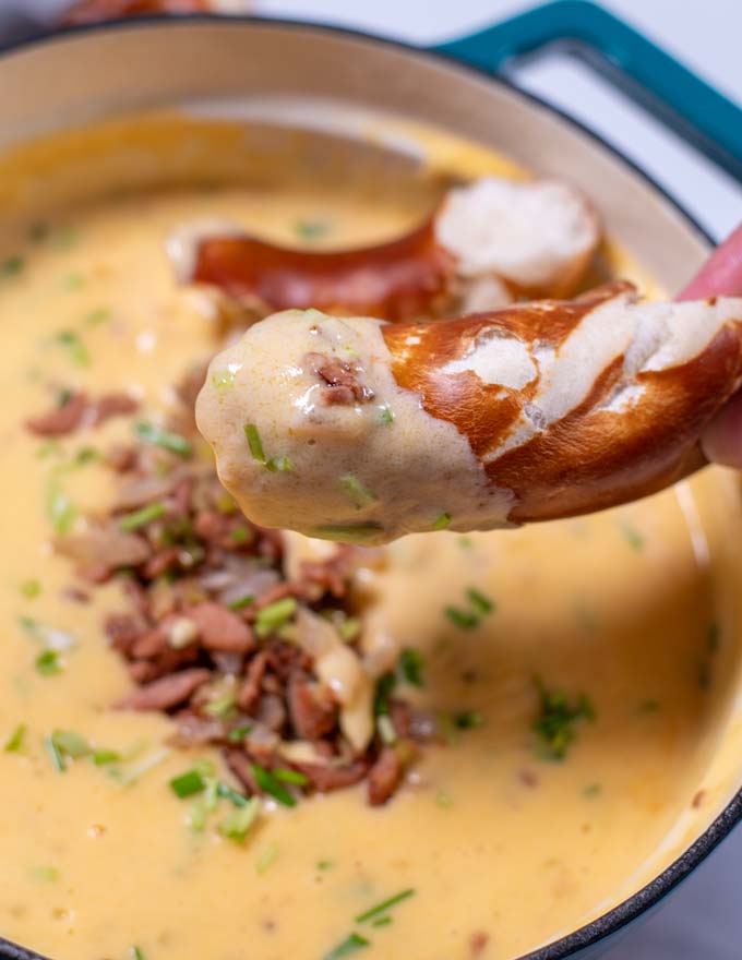 A soft pretzel covered in Beer Cheese Soup is held in hand.