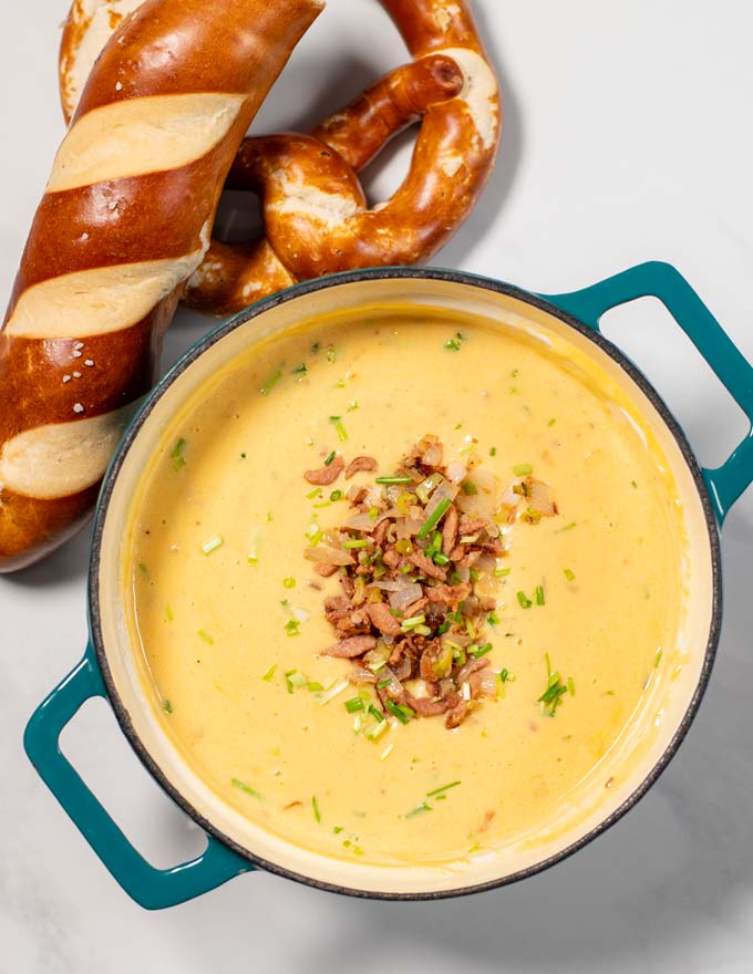 Top view of a large Dutch oven with Beer Cheese Soup and soft pretzels in the background.