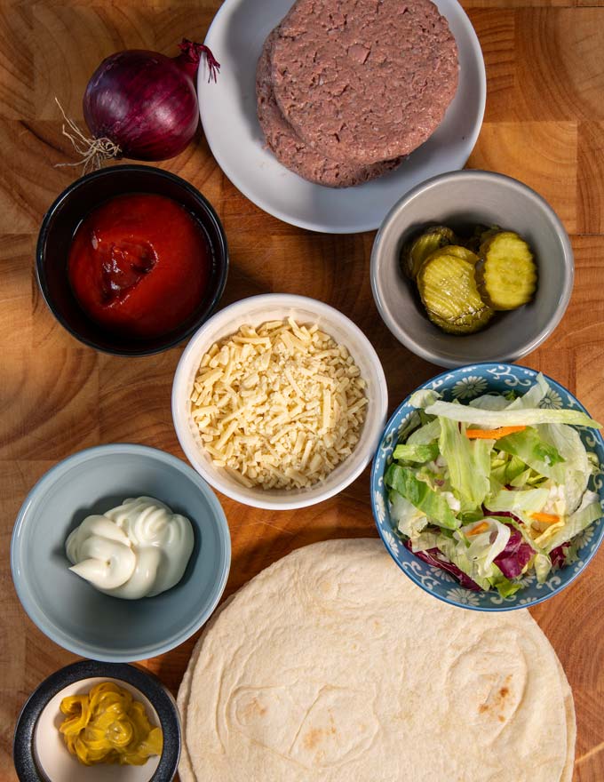 Ingredients needed to make Burger Wraps are collected on a wooden board.