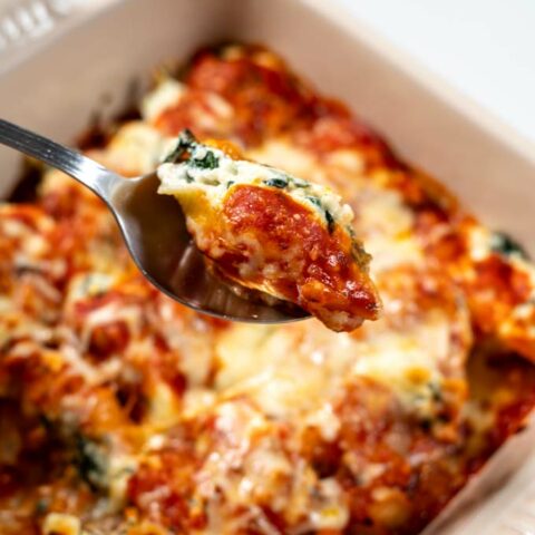 a spoon lift a stuffed shell from the casserole dish.