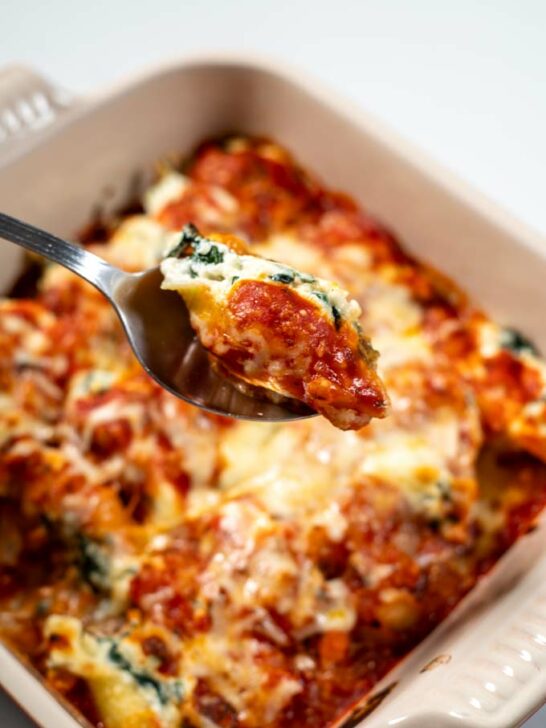 a spoon lift a stuffed shell from the casserole dish.
