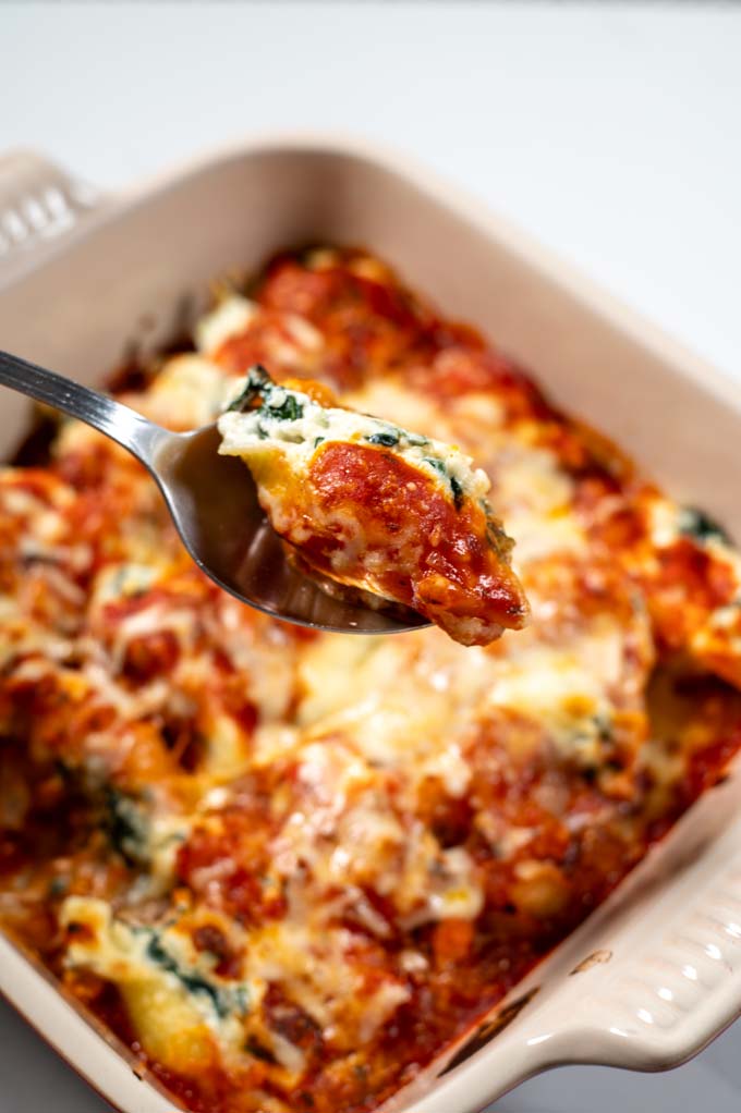 a spoon lift a stuffed shell from the casserole dish.