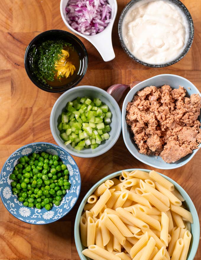 Ingredients needed to make Tuna Pasta Salad are collected on a wooden board.