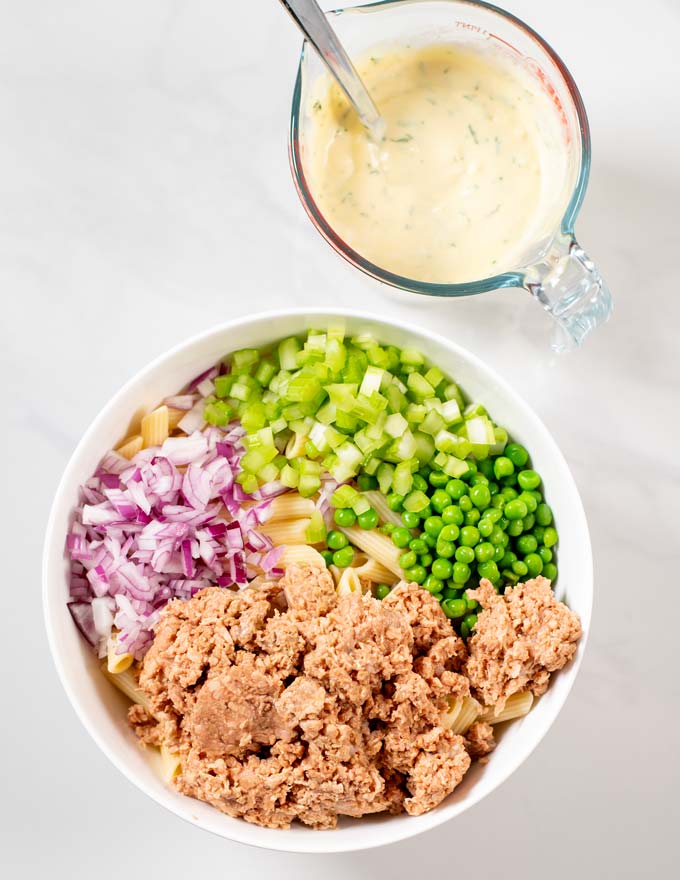 Step-by-step guide for making Tuna Pasta Salad, with all ingredients in a large mixing bowl and a jar with the dressing at the side.