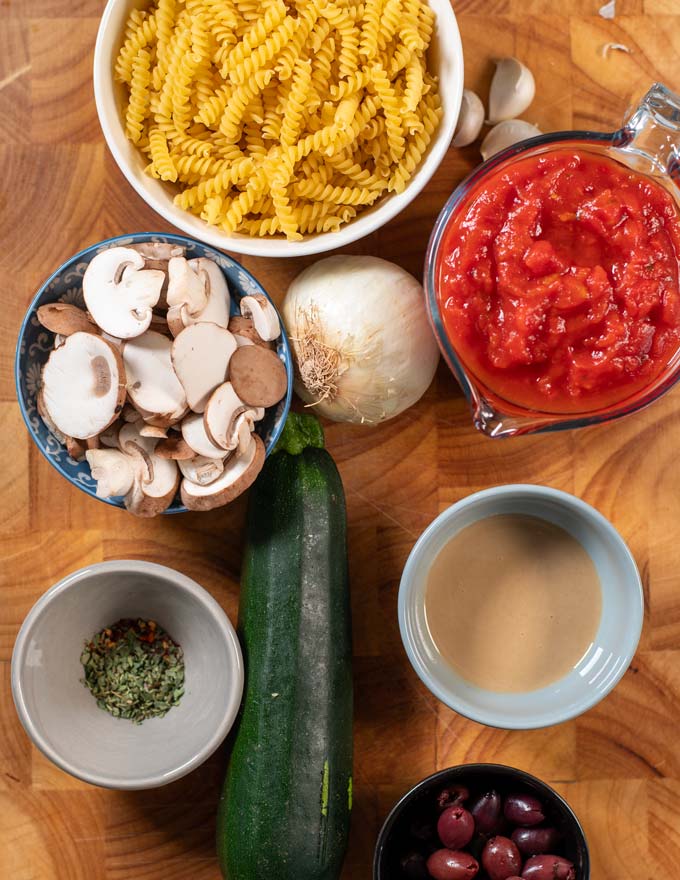 Ingredients needed to make pasta with mixed vegetables collected on a board.