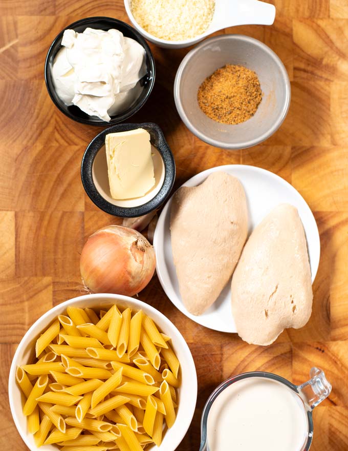Ingredients needed for making Cajun Chicken Alfredo Pasta are collected on a wooden board.