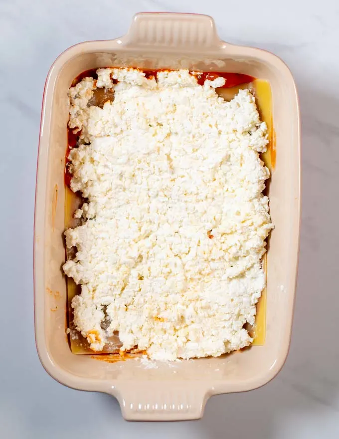 Showing how a layer of ricotta mixture is given onto the casserole dish.