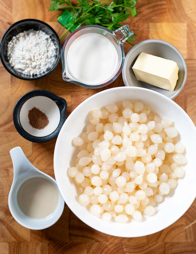 Ingredients needed to make Creamed Onions are collected before preparation on a wooden board.