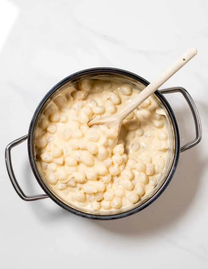 Top view of a saucepan with Creamed Onions and a wooden spoon.