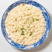 Top view on a serving bowl with Creamed Onions, garnished with fresh herbs.
