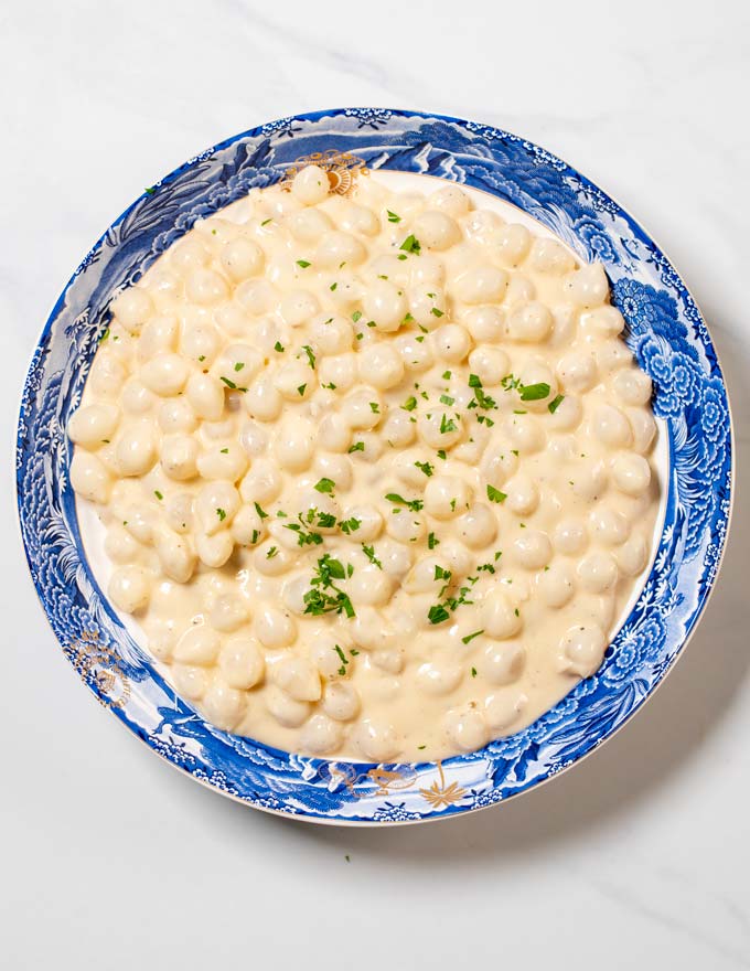 Top view on a serving bowl with Creamed Onions, garnished with fresh herbs.