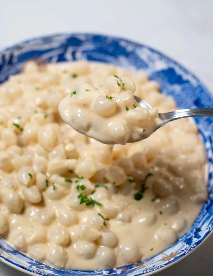 A large spoon of Creamed Onions is lifted from the bowl.