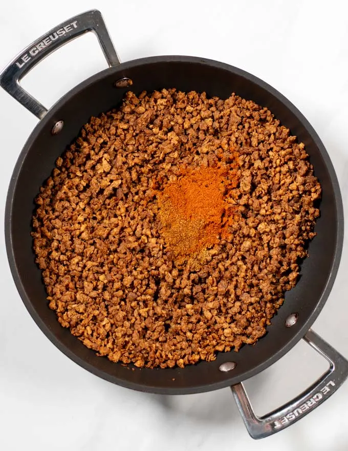 Spices are added to vegan ground beef in a pan.