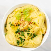 Top view of a serving bowl with Skordalia, garnished with fresh herbs, scallions, and chili flakes,