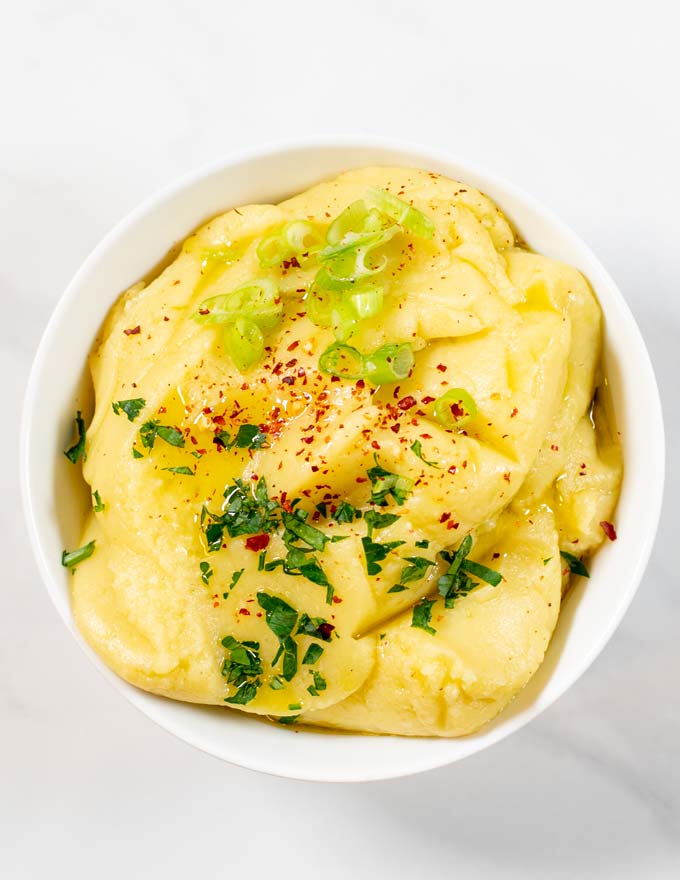 Top view of a serving bowl with Skordalia, garnished with fresh herbs, scallions, and chili flakes.