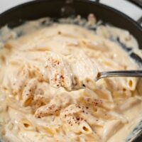 A spoonful of Spicy Alfredo Sauce is lifted from the pan.