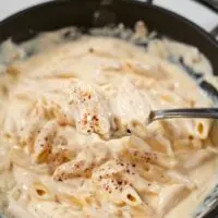 A spoonful of Spicy Alfredo Sauce is lifted from the pan.