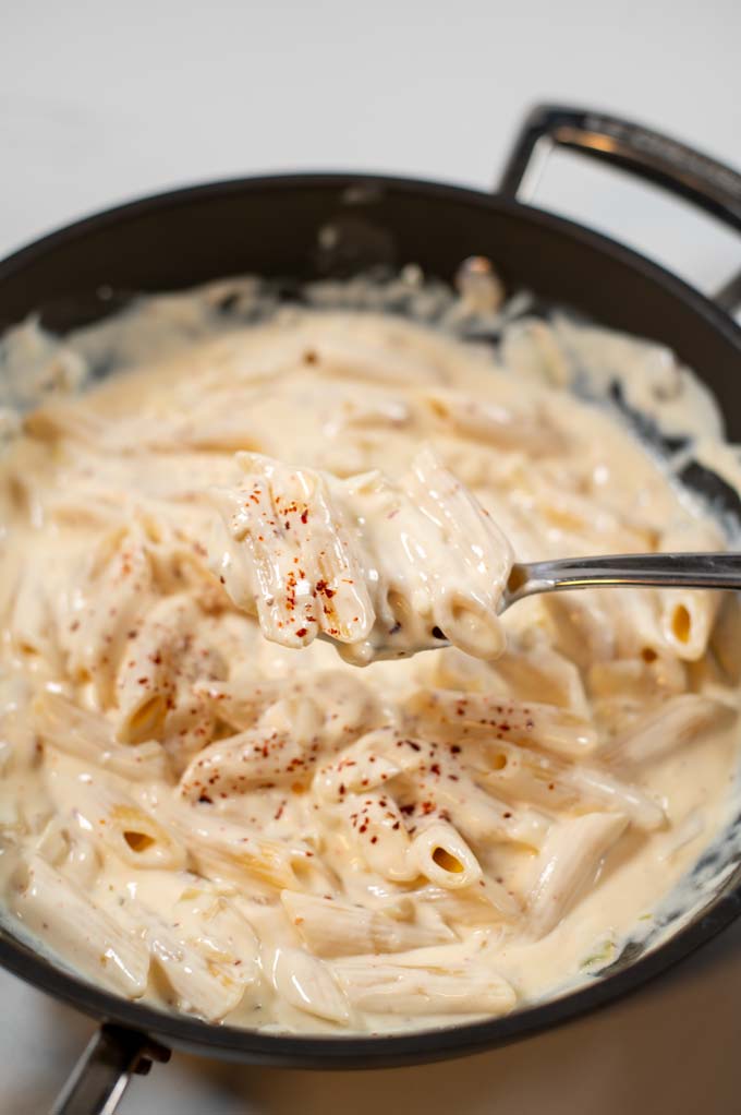 A spoonful of Spicy Alfredo Sauce is lifted from the pan.