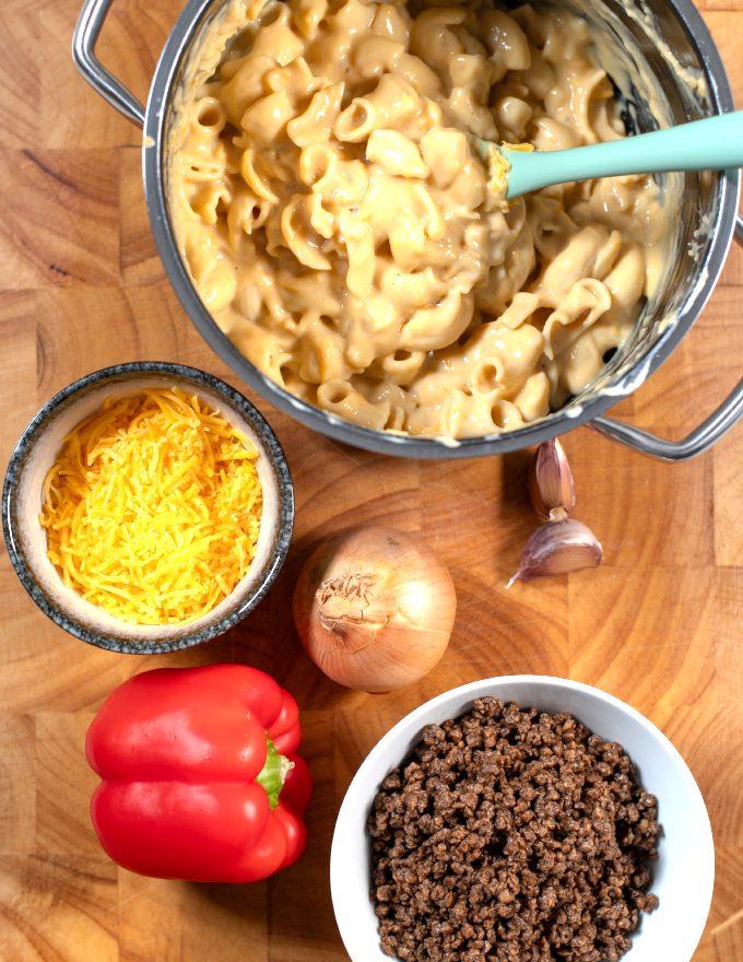 Ingredients needed to make Leftover Mac and Cheese Casserole are collected on a wooden board.