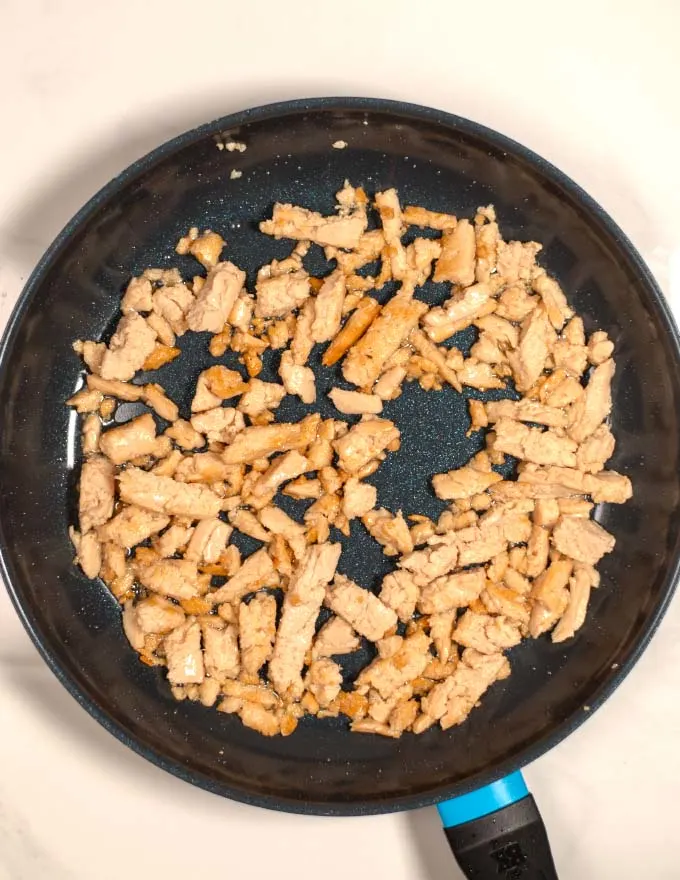 Top view of a large skillet in which vegan chicken pieces are fried in hot oil.