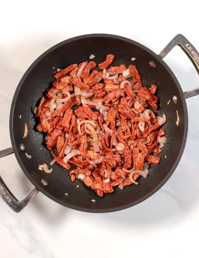 Top view of a saucepan with plant-based bacon bits and shallots.