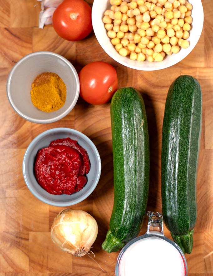 Ingredients needed to make Zucchini Curry are collected on a wooden board.