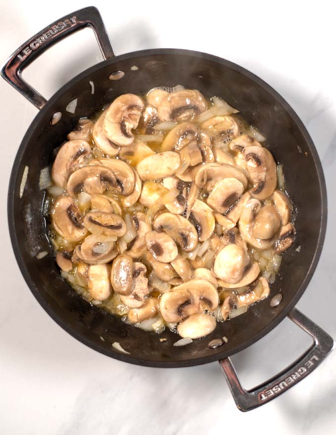 Top view of a large skillet with sautéing mushrooms.