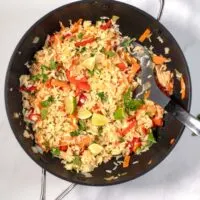 Top view of a large wok with Thai Fried Rice, garnered with cilantro and lime wedges.