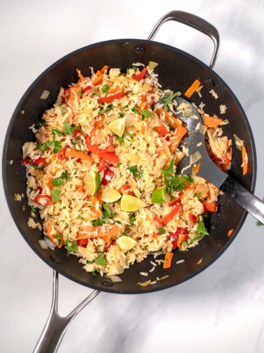 Top view of a large wok with Thai Fried Rice, garnered with cilantro and lime wedges.