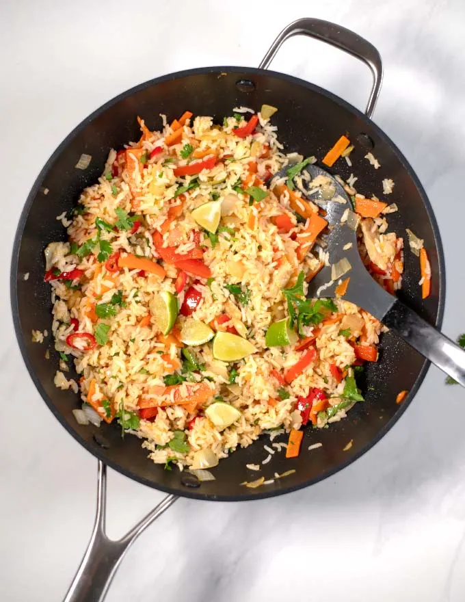 Top view of a large wok with Thai Fried Rice, garnered with cilantro and lime wedges.