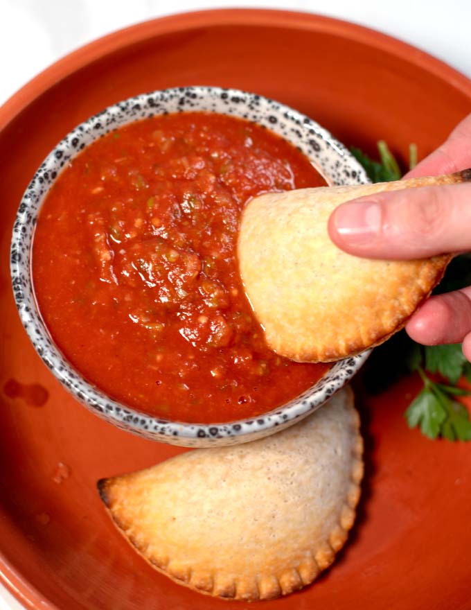 An empanada is dipped into empanada sauce.