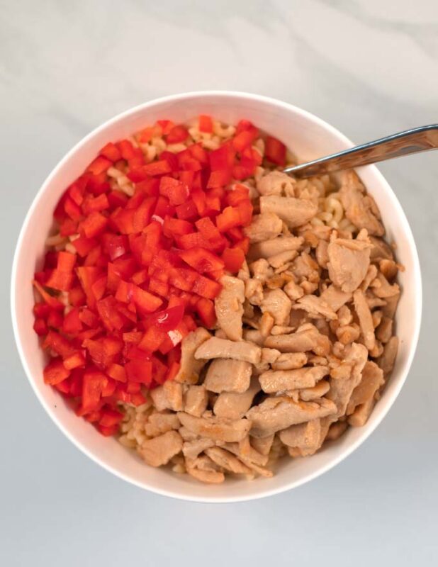 Pasta, red bell pepper, and cooked chicken are added to a large mixing bowl with the seasoned mayo.