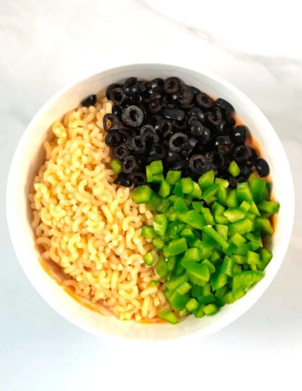 Cooked pasta, sliced olives, and chopped green bell pepper are given to the mixing bowl with the dressing.