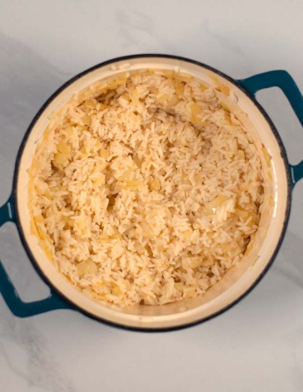 Rice is mixed with the butter onions in a pot.