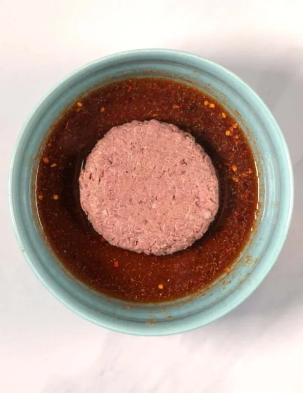 A burger patty is marinated.