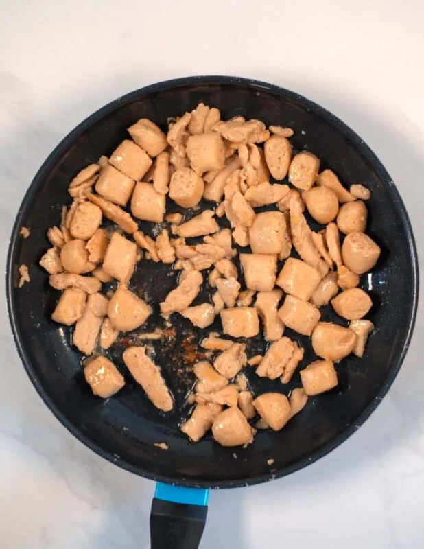 Chicken bits are fried in a pan.