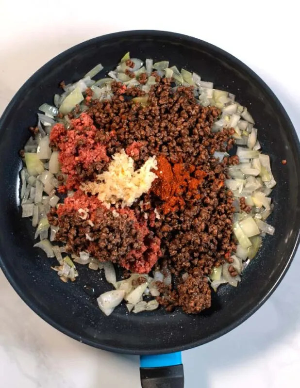 Vegan hamburger meat and seasoning are given to a pan.