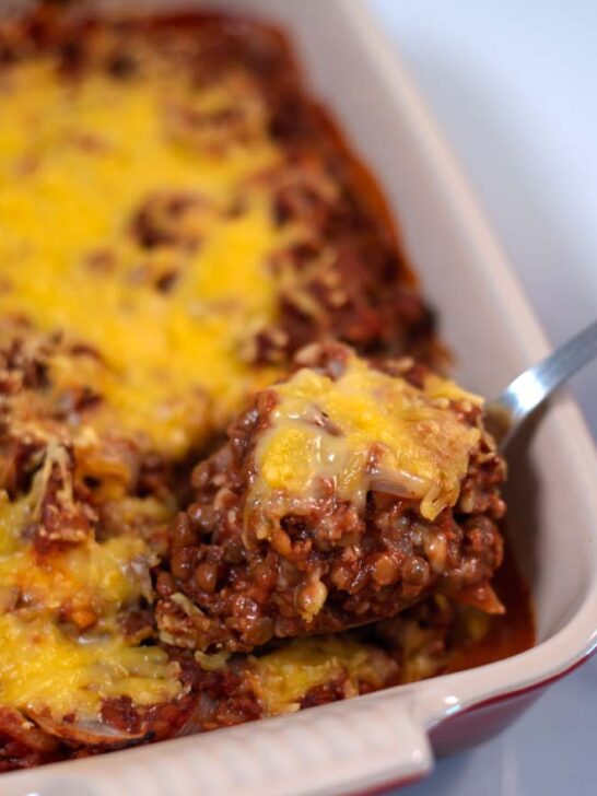 A spoonful of Lentil Casserole is lifted from the baking dish.