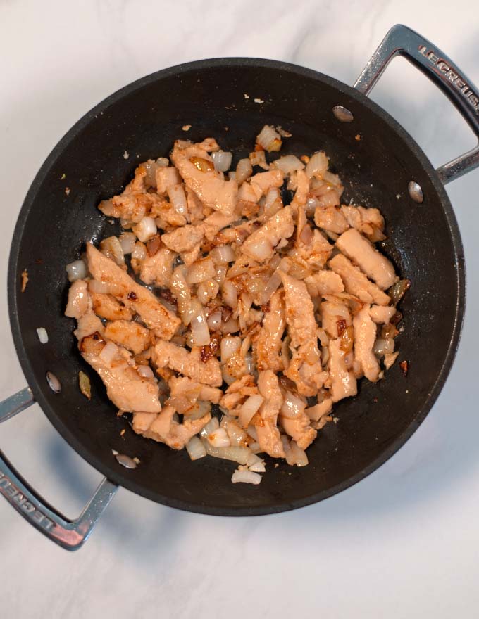 Onions, garlic, and chicken are sauteed in a pan.