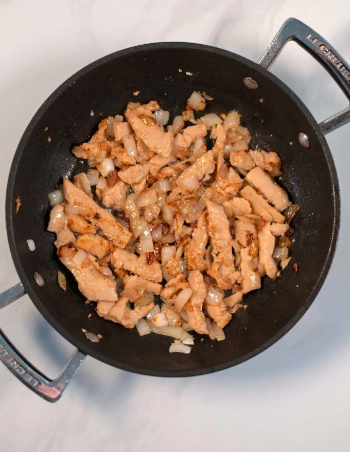 Onions, garlic, and chicken are sauteed in a pan.
