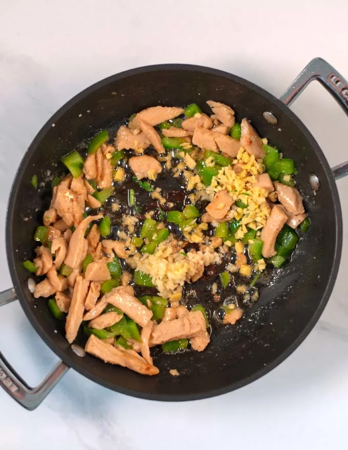 Vegan chicken, green bell pepper is fried in a pan with ginger and garlic.