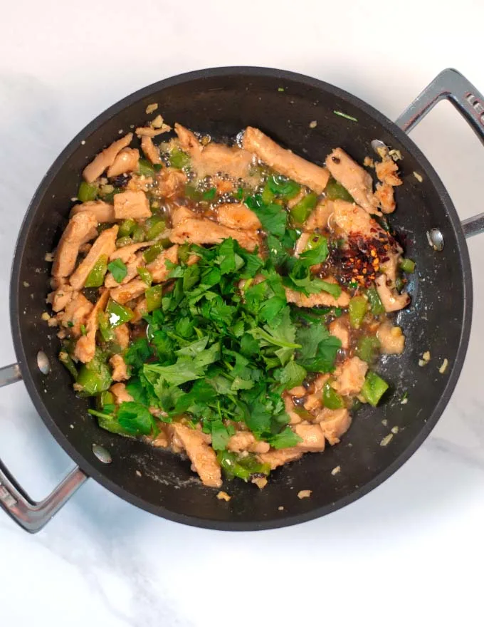 Sauce ingredients and fresh cilantro are given to the stir fry.