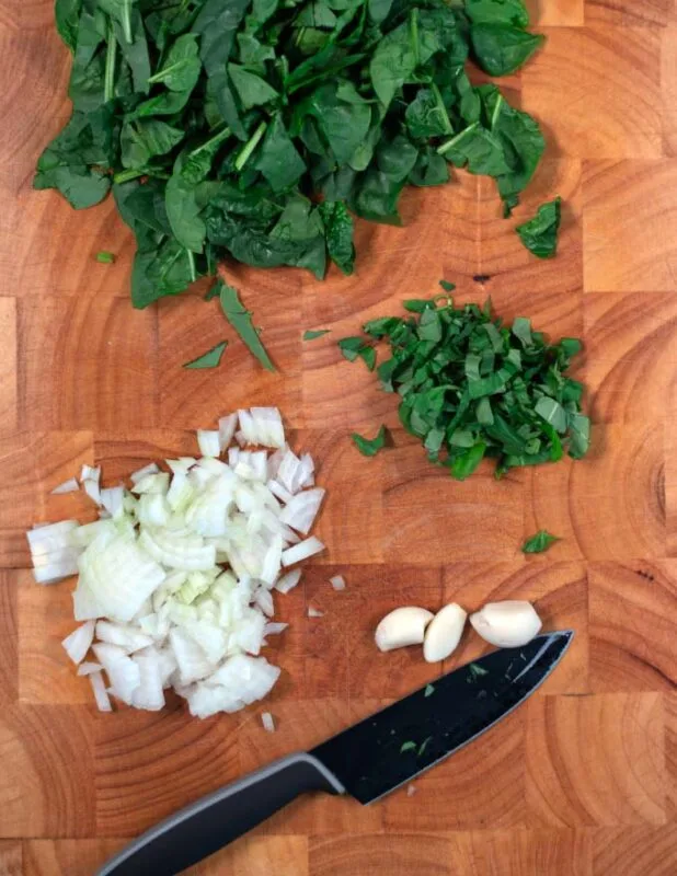 Cutting board with onions, basil, and baby spinach.
