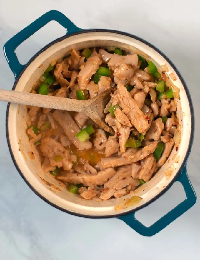 Vegan chicken, green bell pepper and spices are cooked in a saucepan.