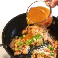 Chinese Orange Sauce is poured over chicken in a pan.