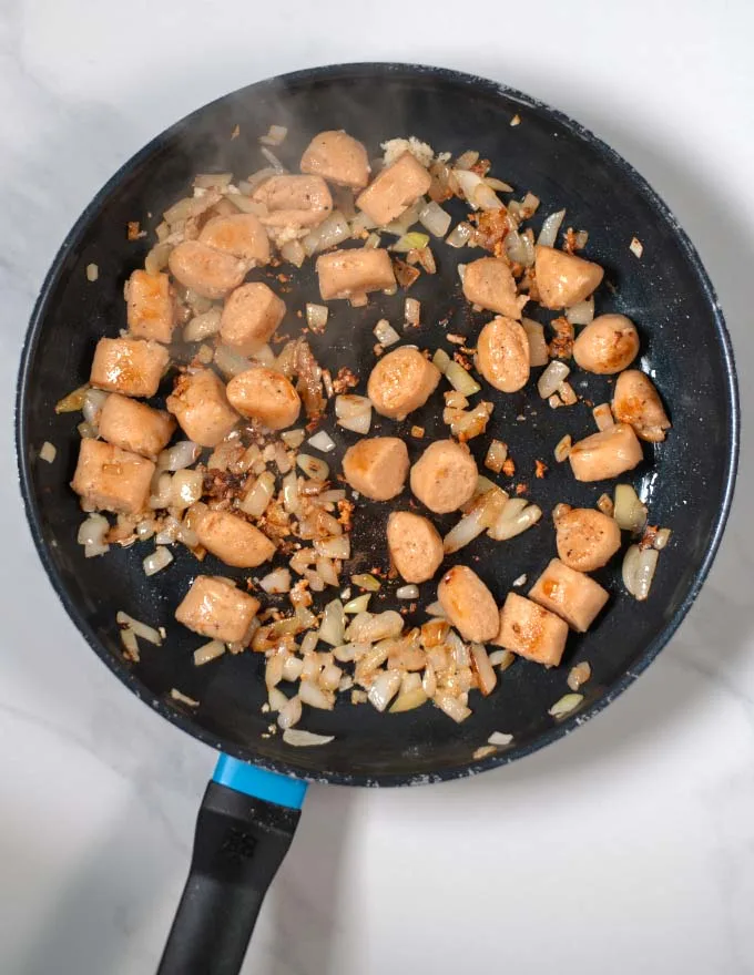Onions and sausage bits are fried in a pan.