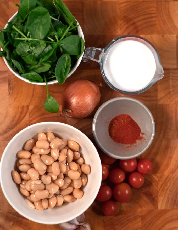 Ingredients needed to make Marry Me Butter Beans on a wooden cutting board.