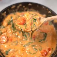 A large spoon lifts Marry Me Butter Beans from a pan.
